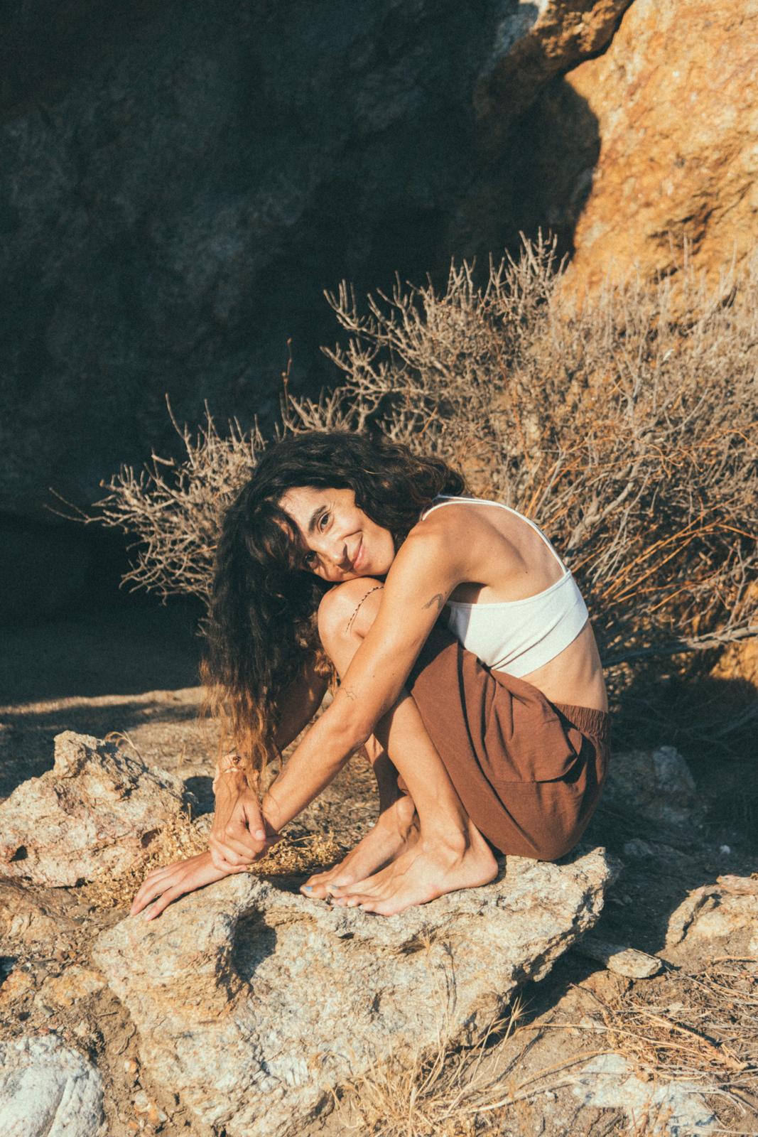 Inês crouched on sunlit rocks, smiling